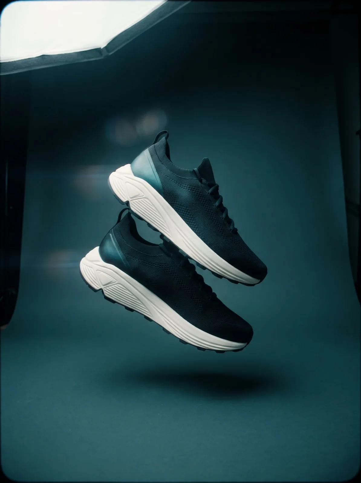 Sneakers svävande i studioljus mot petrolblå fond — exempel på produktfoto